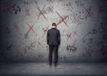 Back view of a businessman lean with his forehead to concrete wall with depicted ideas that crossed by red.の写真素材