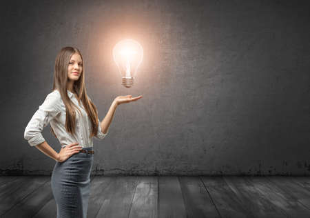 Cropped portrait of a young businesswoman holding big glowing light bulb. Business staff. Office clothes. Ideas and concepts. Inspiration and creativity.の写真素材