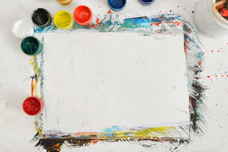 Top view of an artist's workplace with a sheet of paper and jars of different paint.の写真素材