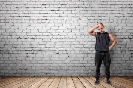 Front view of muscled young man thinking, on the background of white brick wall. Wellbeing. Muscleman. Workout and fitness.の写真素材