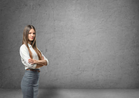 Cropped portrait of a young businesswoman with her arms folded in the background of a concrete wall. Business staff. Office clothes. Successful lifestyle.の写真素材
