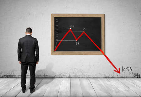 Back view of a businessman standing in front of blackboard with falling diagram that goes down to...