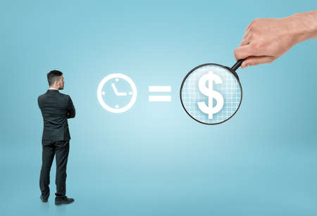 Back view of a businessman looking at sigh 'time is money' with big man's hand enlarging dollar sign with a magnifier. Benefit and success. Wealth and prosperity.の写真素材