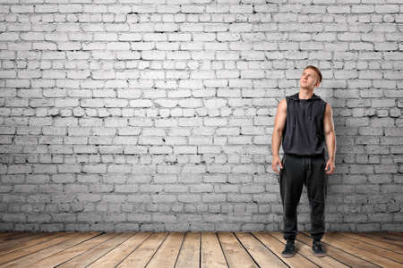 Front view of muscled young man looking up, on the background of white brick wall. Wellbeing. Muscleman. Workout and fitness.の写真素材