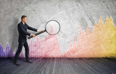 Side view of a businessman looking through a magnifier on colorful diagram. Stock market. Economic...
