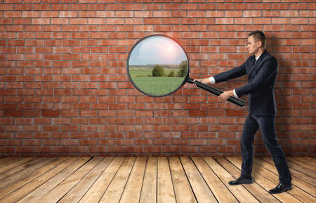 Side view of a businessman looking at red brick wall through a magnifier and seeing nature landscape. Ideas and concepts. Solution and way out. Inspiration.の写真素材