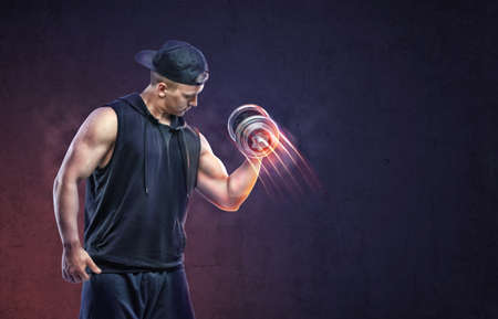 Muscular young guy lifting a dumbbell to training his biceps. Power training. Healthy lifestyle. Fitness and sport. Biceps Exercises.の写真素材