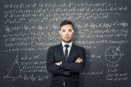 Businessman standing on the background of blackboard with mathematical formulas. Science and education. Mathematics, algebra and geometry.の写真素材