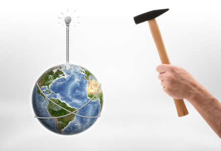 Close up view of a man's hand driving a nail into wall with the Earth hunging on it isolated on white background. Ecology and environment. Natural resources. Elements of this image are furnished by NASA.の写真素材