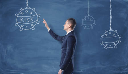 Businessman looking at the naval mines and the word 'risk' drawn with chalk on the dark blue wall. Face serious challenges. Difficulties and problems in business. Bold experiments.の写真素材