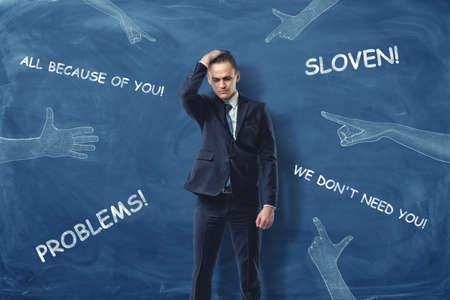 An embarrassed businessman standing and running his hand through his hair near the dark blue wall...