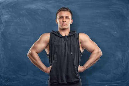 Muscular young man in sportswear standing on the dark blue background. Sport and healthy lifestyle. Keep fit. Athletic body.の写真素材