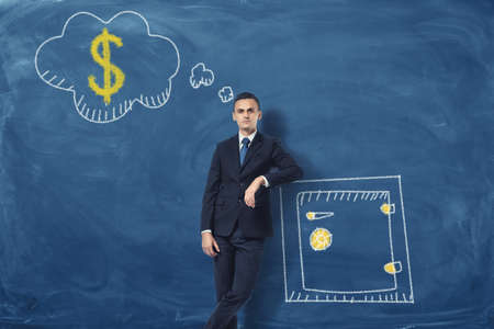 A businessman leaning on a drawn safety box and thinking about money on blue chalkboard background about money. Savings and investment. Business development. Make profits.の写真素材