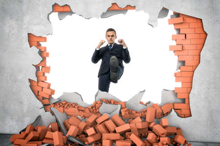 Businessman ruins a brick wall with his leg isolated on the white background. Decisive actions. Brandnew business ideas. Destruction of impediments.の写真素材