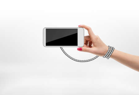 Woman holding mobile phone with drawn rope wrapped around her hand on white background. Modern technologies. Cell phone addiction. Electronic means of communication.の写真素材