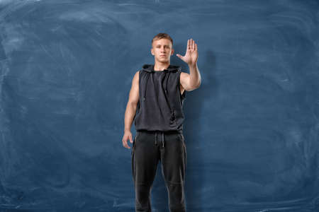 A muscular young man standing and making stop sign with hand on the blue chalkboard background....