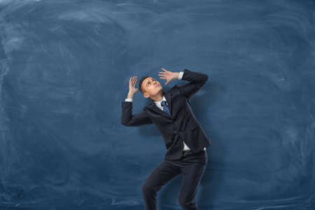 Businessman standing in desparate pose on blue chalkboard background. Problems and issues. Protection and defense. Psychological burden and stress.の写真素材