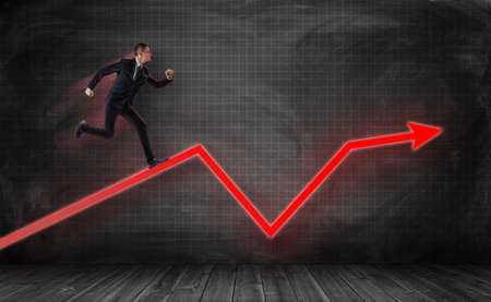 A small businessman running on a huge red kinked arrow on a dark plaid background. Aspiration to success. Business improvement. Positive trend.の写真素材