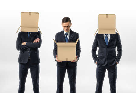 Businessmen holding an open cardboard box, the other two are wearing the boxes on their heads. Anonymous person. Packing and crating. Business and management.の写真素材
