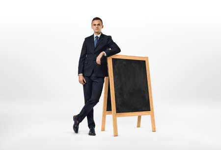 Businessman with a serious face leaning on the small blackboard isolated on the white background. Lack of ideas. Business development. Business learning.の写真素材