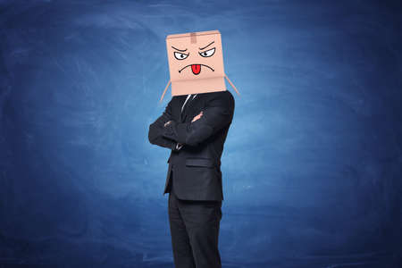 Businessman wearing carton box with painted angry face showing tongue on it