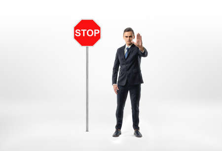 Businessman standing on white background making stop hand gesture with traffic sign beside him.の写真素材