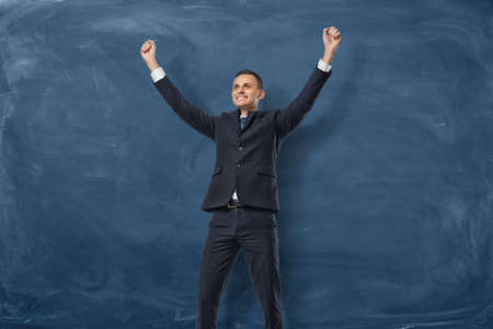 Businessman with hands raised in victory on dark blue blackboard backgroundの写真素材