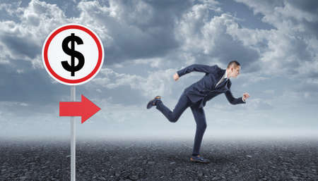 Businessman running on asphalt and road sign with dollarの写真素材