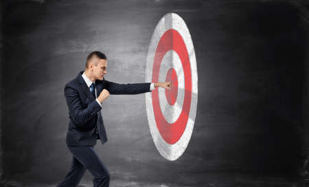 Businessman is hitting with fist target on black background of concrete wallの写真素材