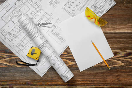 Blueprints on wooden background with piece of paper, compass, pencil, measuring tape and protective glasses.の写真素材