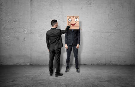 Businessman is drawing happy face on box which hides another mans headの写真素材