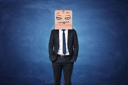 Businessman wearing cardboard box with drawn thoughtful face on his headの写真素材