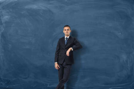Young businessman is leaning to copy space on the blue chalkboard backgroundの写真素材