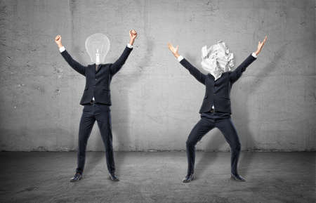 Two businessmen on concrete background, one has a lamp in pace of his head, and another has a white ball of paper.の写真素材