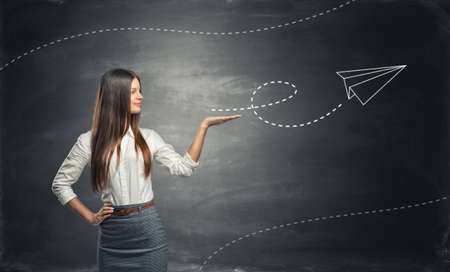 Young lady in official clothing is launching a paper airplane resembling to an arrow on the blackboard backgroundの写真素材