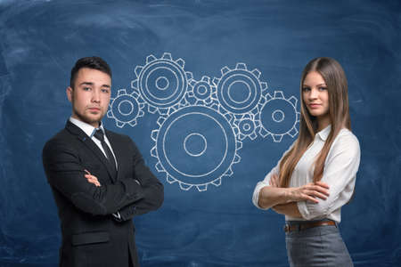 Businessman and businesswoman with gear wheels work in team on blue backgroundの写真素材