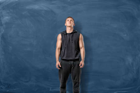 Fit man in black standing on blue chalkboard background and looking up.の写真素材