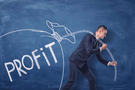 Businessman is pulling a big drawn bag of money on a rope on the blue backgroundの写真素材