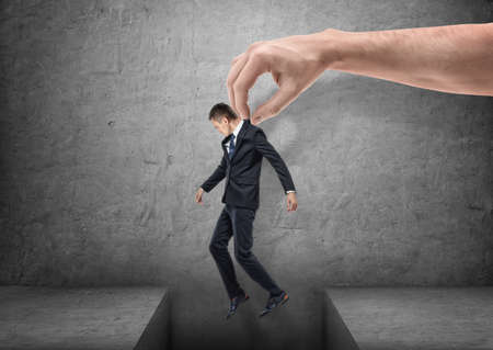 Big hand is bringing a businessman over a gap in the floor on gray backgroundの写真素材