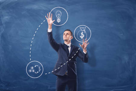 Businessman on blue chalkboard background manipulating white see-through icons that are connected with dash lines.の写真素材