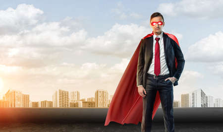 A businessman in superhero mask and cape on the sky background with many apartment blocks in the distance.の写真素材