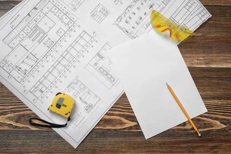 Blueprints, pencil, protective glasses, steel tape, pencil and white paper lying on wooden table background.の写真素材