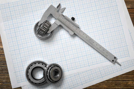 A large vernier scale lying on cross section paper with three bearings around it on wooden background.の写真素材