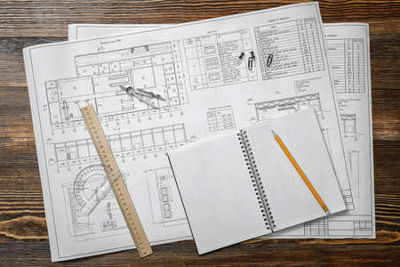 Open blueprints on wooden table background with a pencil, a ruler and compasses lying beside.の写真素材