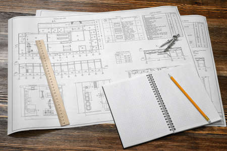 Open blueprints on wooden table background with a pencil, a ruler and compasses lying beside.の写真素材