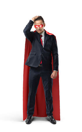 A businessman in a formal suit and superhero cape and mask looking doubtful and holding his head.の写真素材