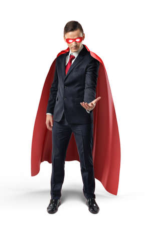Businessman in a red cape and red eye mask looking at his hand and holding something on white background.の写真素材