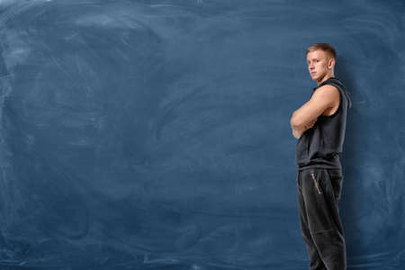 Muscular young man is standing his arms crossed and looking forward on blue chalkboard backgroundの写真素材