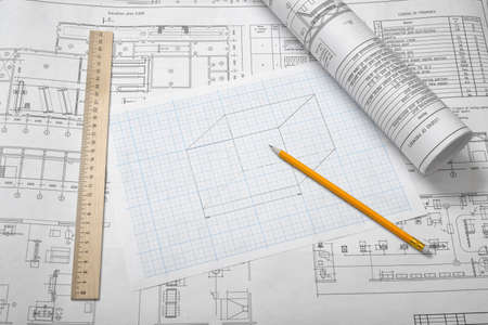 A set of open and rolled up blueprints on wooden table background with a pencil and a ruler lying beside.の写真素材