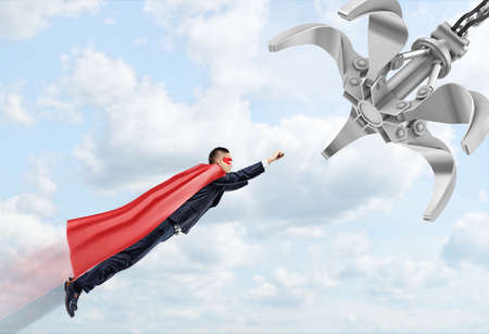 A businessman wearing a red superhero cape flying through the clouds following a robotic manipulator.の写真素材
